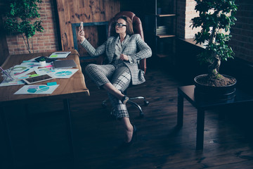 Obraz premium Full length body size photo beautiful amazing she her business lady look telephone smart phone make take selfies sit big cozy comfort chair near window sill office formal wear checkered plaid suit