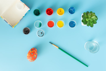 Preparing for Easter multicolor paints and Hand made colored egg next to brush on a blue bacground Easter concept