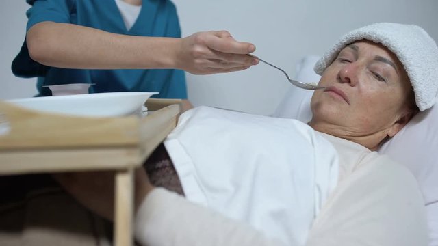 Terminally ill woman with compress on forehead refusing from hospice porridge