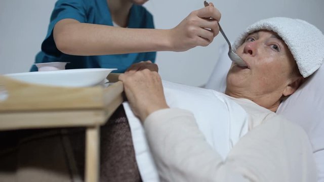 Nurse of mental hospital feeding indifferent woman with porridge, asylum