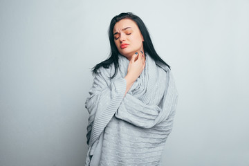 An upset girl in a gray plaid is experiencing pain, sore throat, pain in the thyroid, flu, or osteochondrosis. Upset ill woman on gray studio background.