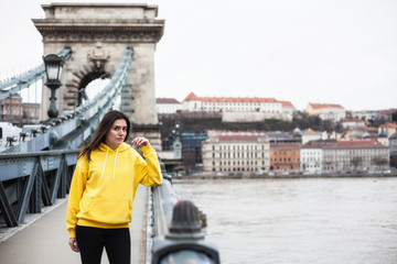 Stylish young woman in yellow hoody posing in the city streets. Urban style woman