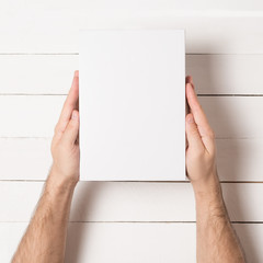 Obraz premium White rectangular box in male hands. Top view. White table on the background