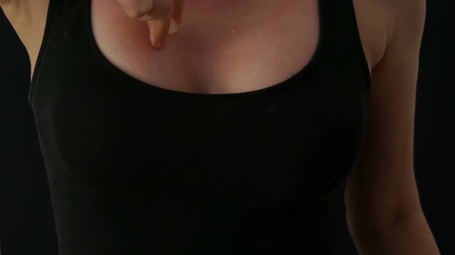 Women's hands are sexually rubbing ice cubes over the skin of her breast in a black T-shirt against a black background. Drops of water run down for women's neckline