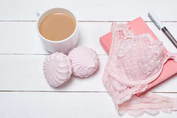 Cup of coffee with marshmallows. Pink lace bodice and notepad on white background. Fashionable concept.