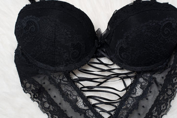Black bodice with lacing on white fur. Flat lay. Fashion lingerie concept.