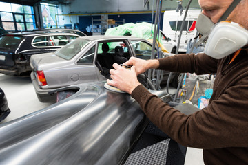 Professioneller Autolackierer schleift ein Autoteil mit der Schleifmaschine vor in einer Werkstatt...