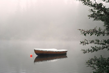 A row boat anchored on the calm lake in the foggy autumn.