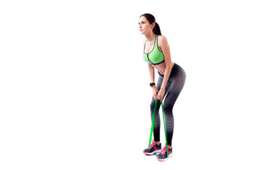 A dark-haired woman coach in a sporty pink short top and gym shows the correct squatting technique with sport fitness rubber bands on a  white isolated background in studio