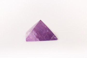 Ametista, primo piano di una pietra preziosa intagliata a forma di piramide con lo sfondo bianco,...