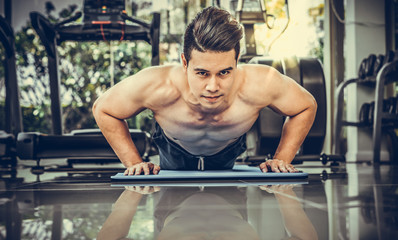 Naklejka na ściany i meble Young man bodybuilder doing push up in fitness center. Healthy lifestyle and body building concept.