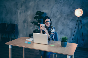 Fototapeta na wymiar Portrait of her she nice attractive cheerful cheery brunette lady in checked shirt sitting in front of laptop having rest time at industrial loft style interior work place station indoors