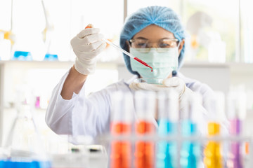 Female scientist dropping red liquid into beaker..