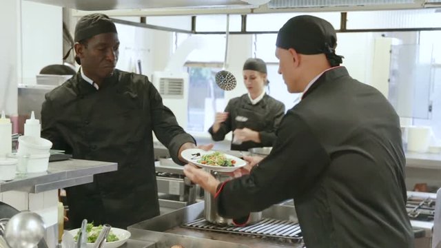 Attractive young waitress taking prepared dishes from chef in kitchen of modern restaurant 