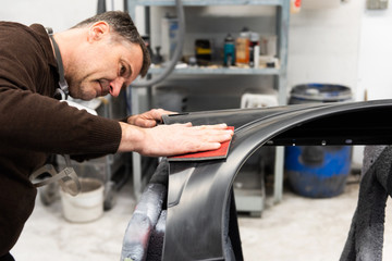 Professioneller Autolackierer schleift ein Autoteil mit Schmirgelpapier vor bei in einer Werkstatt - Serie Autowerkstatt.