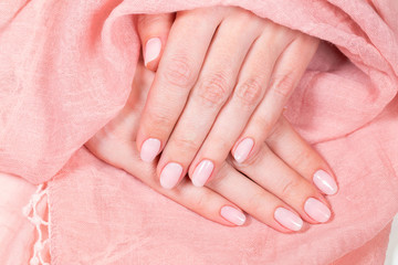 Naklejka premium Top view closeup photography of beautiful female hands isolated on soft pink elegant fabric texture background. Fingernails with fresh professional light pink color manicure.