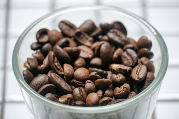 Coffee beans in a glass bowl on white checkered tiles.