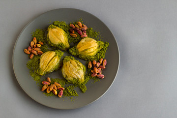 Mussel shaped special Turkish baklava in the grey color round plate with pictachio nuts.Top view and left space for any text message.Conceptual design of Islamic Feasts. 