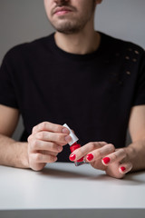 Bearded man holding red nail polish in his hands. Red painted nails. Lifestyle photo. Lgbt community. Transsexual guy.