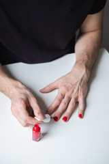 Man with a beard making manicure for himself, holding red nail polish. Lgbt community. Transsexual guy.