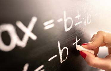 Math teacher writing function, equation or calculation on blackboard in school classroom. Student...