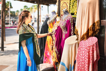 Woman in souk. Tourist looking at traditional Arabian dresses and clothes in store or outdoor...