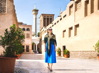 Woman walking in old Dubai, UAE. Traditional Arab street and mosque. Female tourist in historical Al Fahidi neighbourhood wearing dress. Tourism in heritage district. Happy vacation lifestyle.