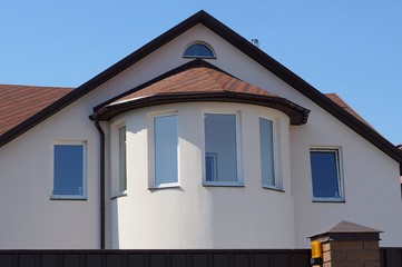 facade of a large house with a loft and windows and brown tiles on the roof against the sky