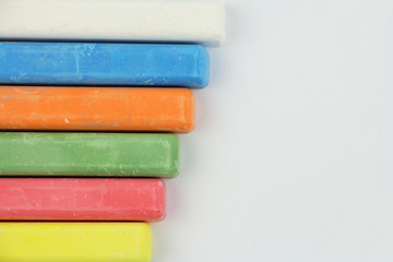 six colored children crayons on white background, on left side, blue red green yellow orange white, top view