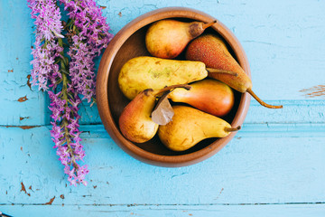 Fresh pears in a wooden plate, flowers Dactylorhiza on an old wooden blue background