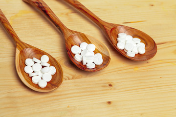 Medicine capsules, pills on wooden spoon background