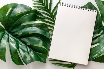 White open notebook with space for text on large green leaves. Mockup with monstera leaves