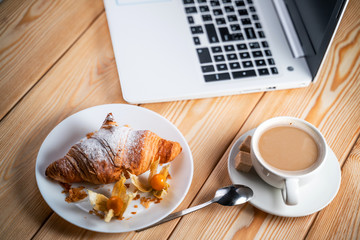 Computer, Cup Coffee and Croissant on brown wood table