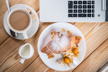 Light lunch in office. Coffee and croissant near keyboard