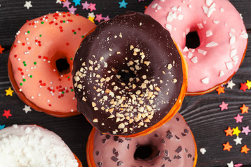 Assortment of colorful donuts decorated with colorful confetti sprinkles on dark wooden background