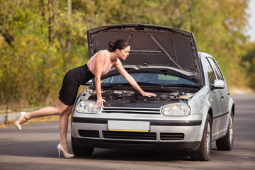 Young woman looks under the hood of his car and trying to find the cause of breakage