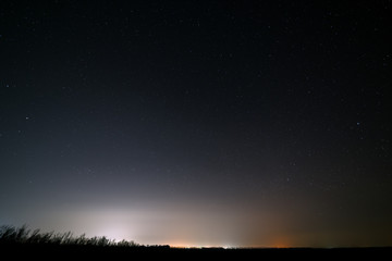 Bright stars in the night sky with lighting from the street lamps of the city. Light pollution.