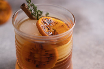 Close up of Whiskey sour cocktail with tangerine slices and ice cubes decorated with cinnamon and thyme.