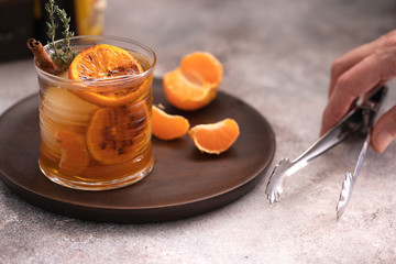 Whiskey sour cocktail with tangerine slices and ice cubes decorated with cinnamon and thyme. Alcohol drink background.