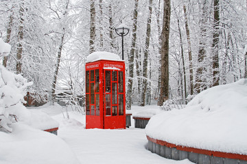 Red British telephone booth used as street library in winter (translated from Russian 