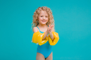curly little blonde girl in a blue swimsuit and yellow swimming armbands