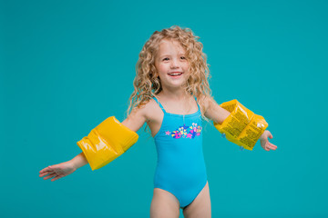curly little blonde girl in a blue swimsuit and yellow swimming armbands