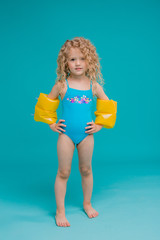 curly little blonde girl in a blue swimsuit and yellow swimming armbands