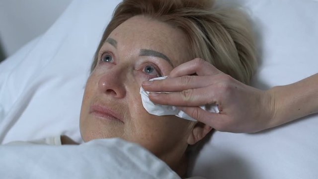 Daughter wiping tears from mothers face, taking care of parent in hospital