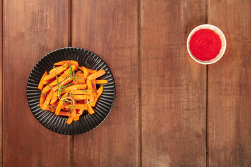 Sweet potato fries with rosemary and tomato sauce, shot from the top on a dark rustic wooden background, forming a frame for copy space