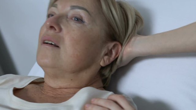 Nurse helping old woman to lay in hospital bed, lady feeling weak after surgery