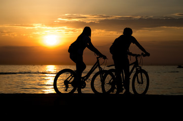 Side view of couple standing on seashore with their bicycles and enjoying sunset