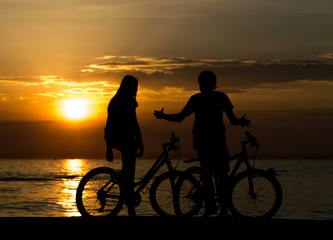 Fototapeta na wymiar Side view of couple standing on seashore with their bicycles and enjoying sunset