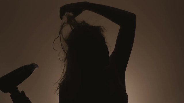 Silhouette of a woman who dries hair with a hair dryer after washing her hair.