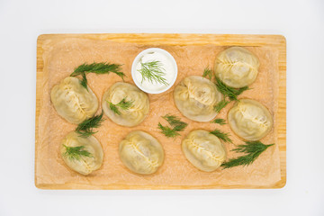 Oriental dish large dumplings "Manty", laid out on a wooden tray with white sauce.